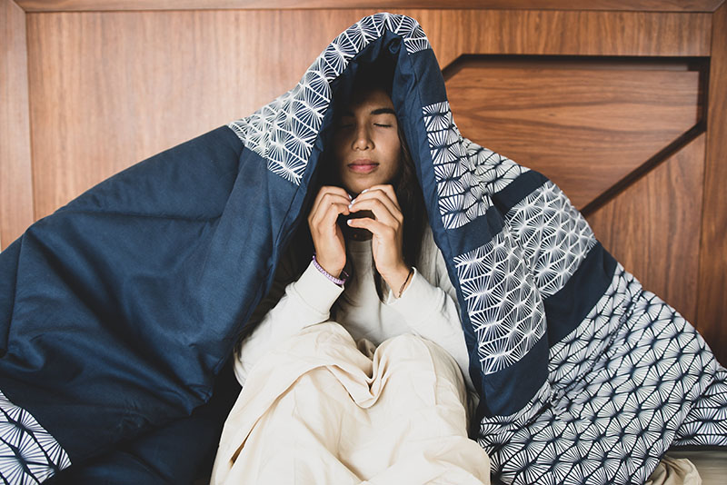 Tired woman under a cozy comforter trying to gather enough energy to face the day; photo by Pexels Los Muertos Crew